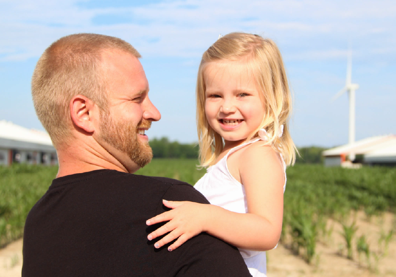 Father holding daughter smiling in front of farming field