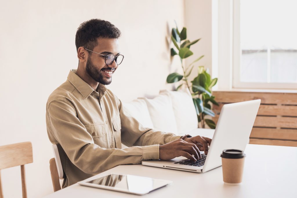 Man sitting at table typing on laptop with coffee and tablet nearby