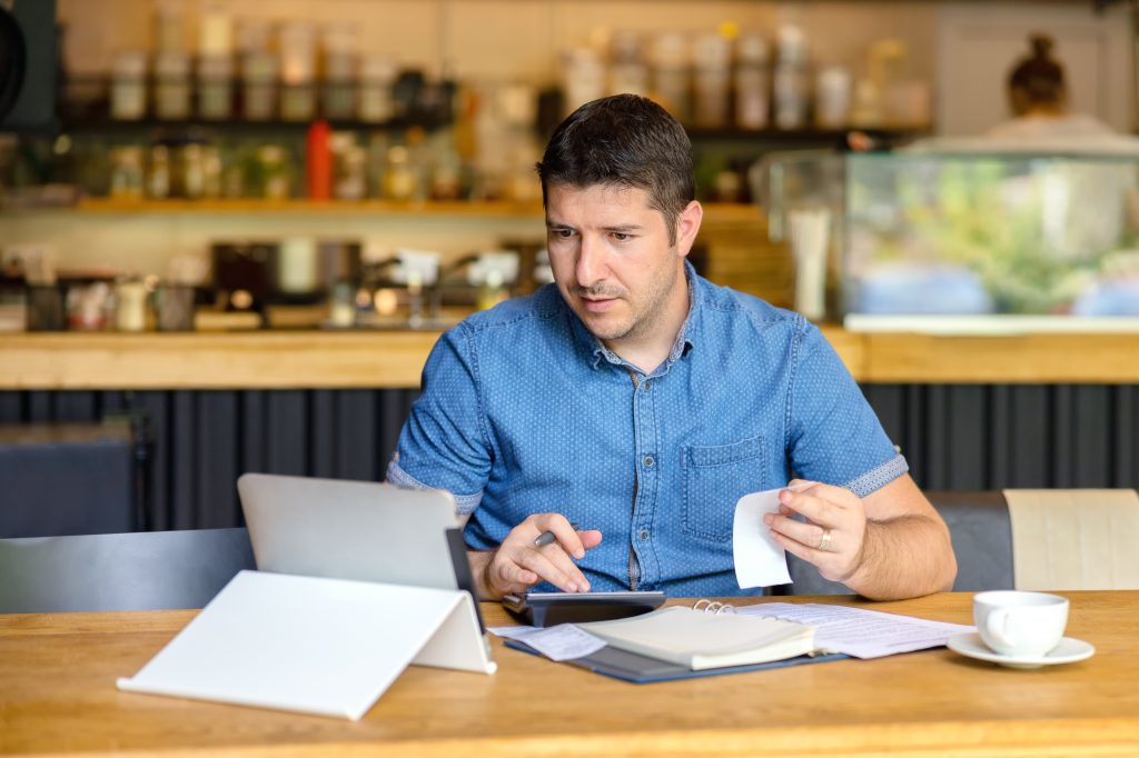 Man at table looking at iPad, calculating finances