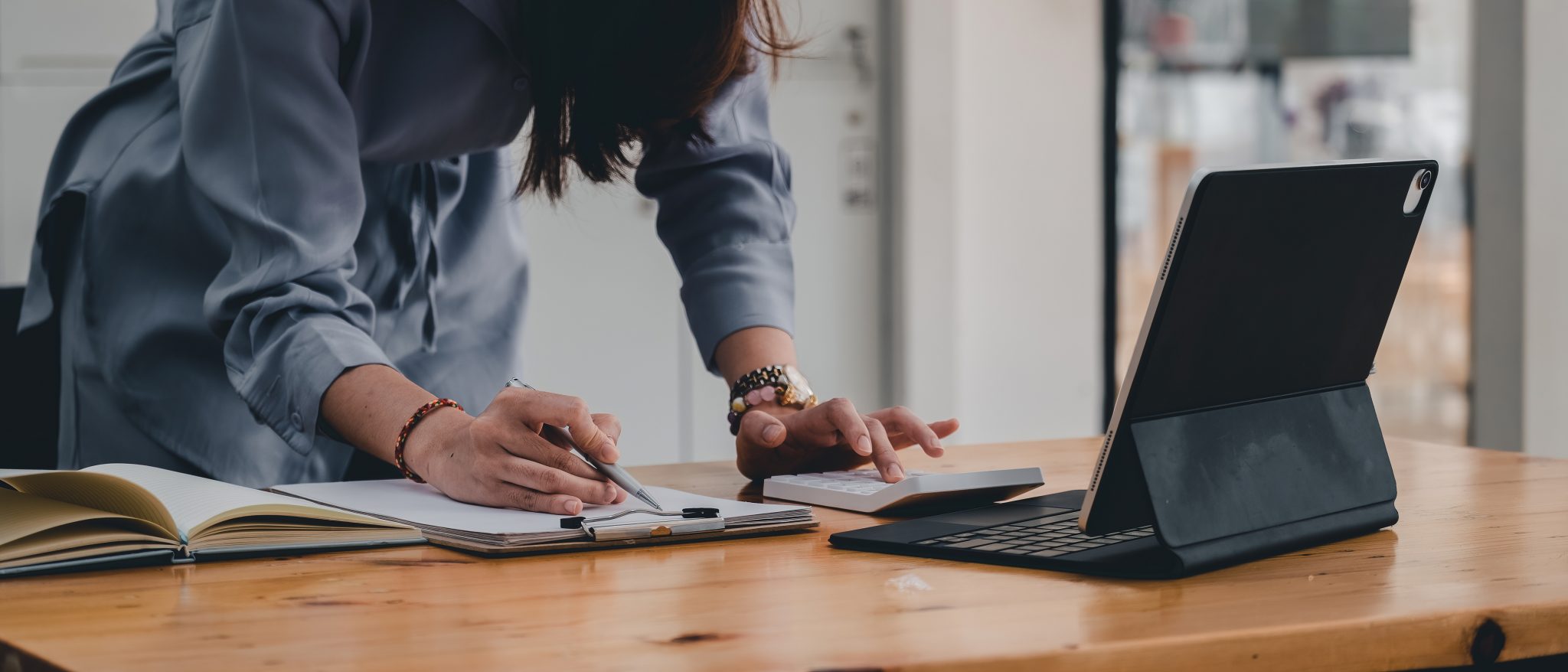 businesswoman or accountant taking note and working on calculator and laptop computer to calculate business data during make note at notepad, accountancy document at office