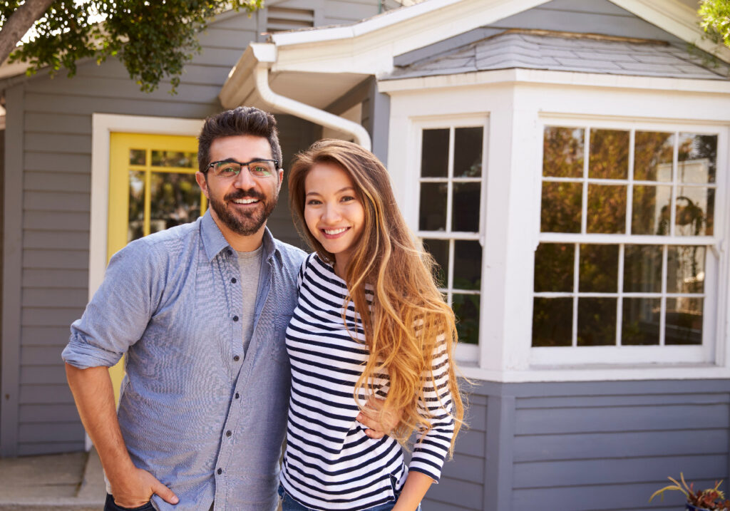 Couple smiling standing in front of a grey house