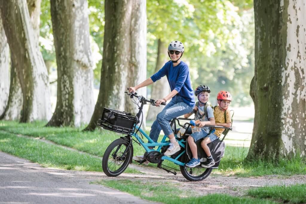 a parent riding a cargo bike with her two kids