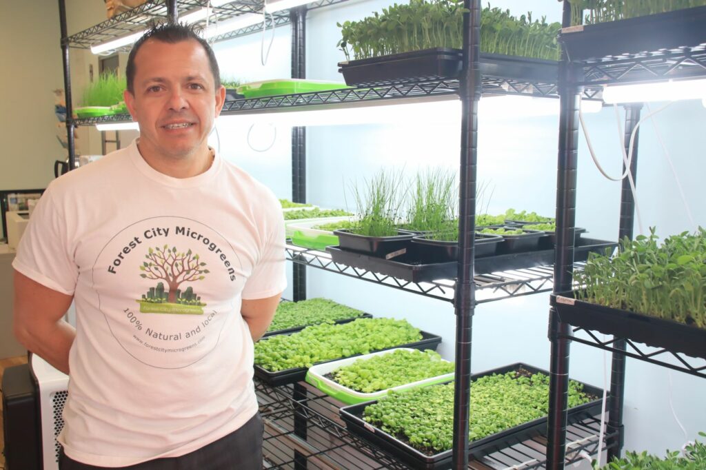 An individual smiling in front of greenhouse grown plants