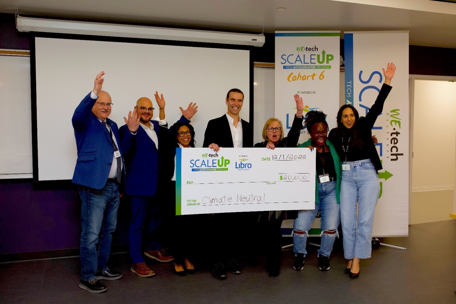 A group of people holding a giant cheque with their arms in the air