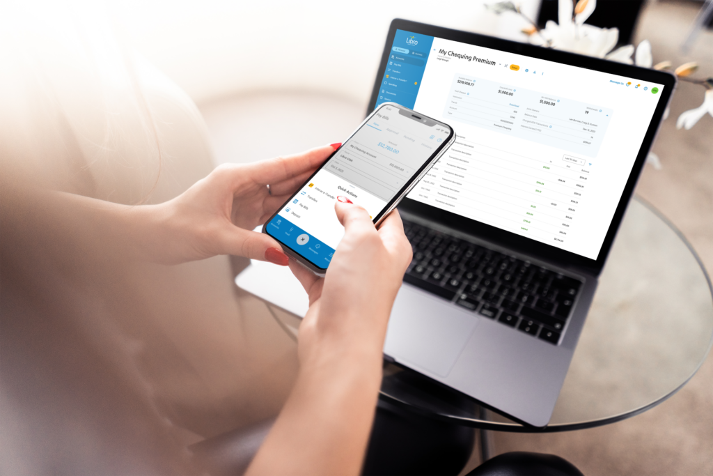 A person holding a cell phone working on a laptop