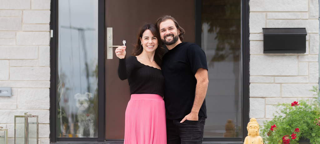 A couple standing in front of their home holding up a house key