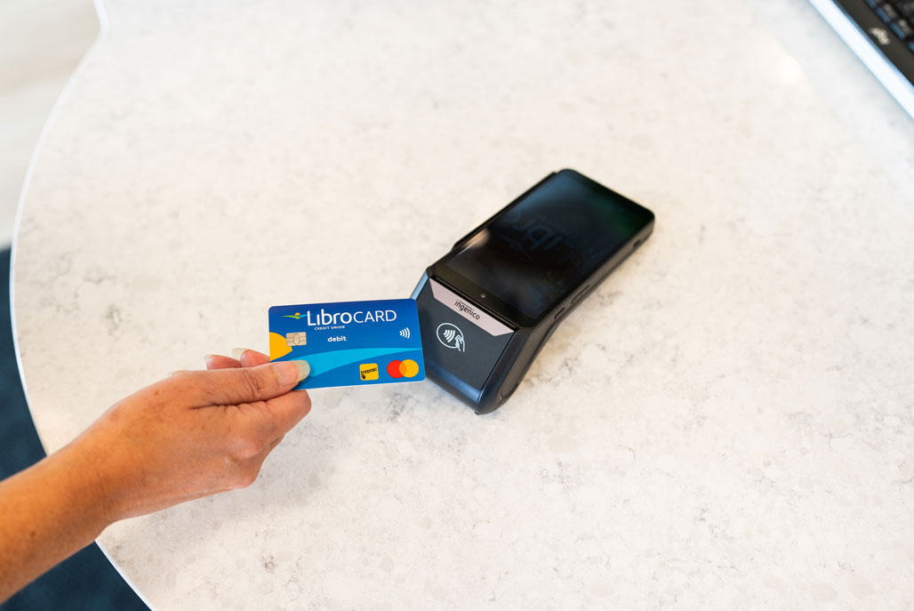 A person holding a Libro card onto a debit machine