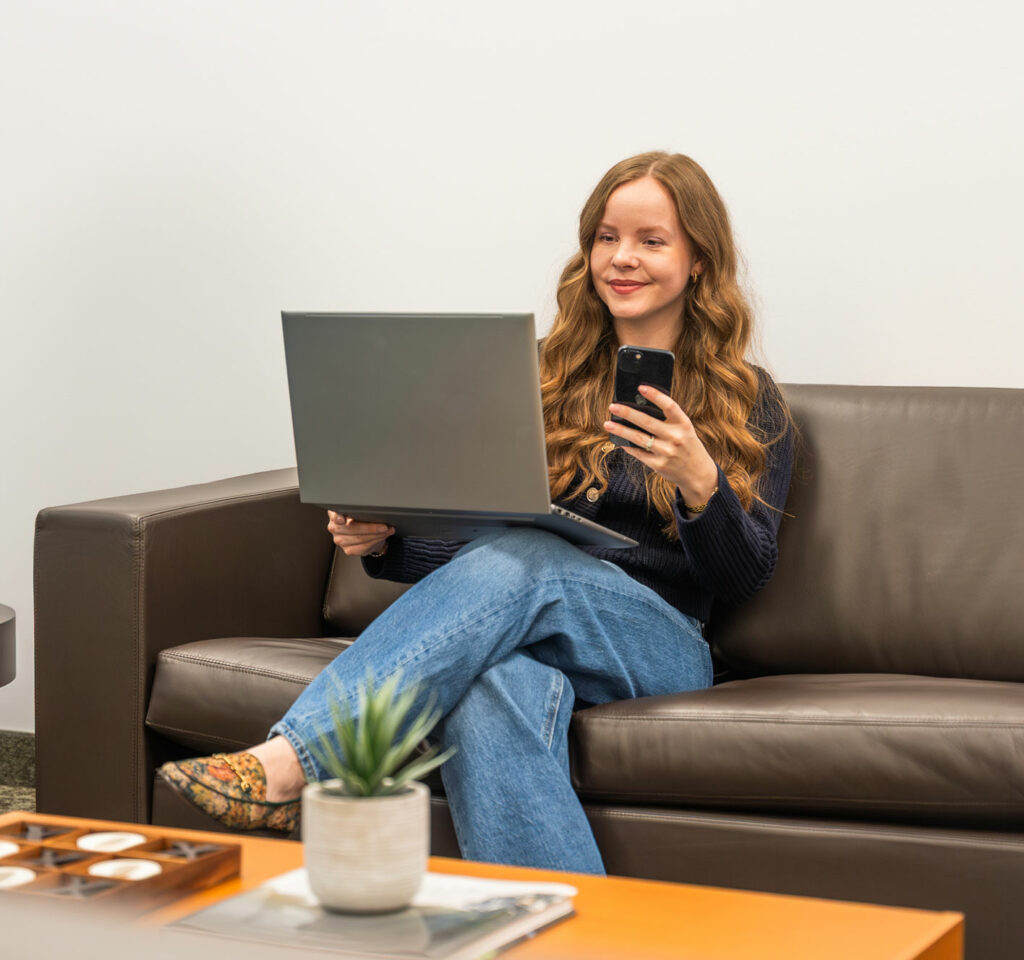 A woman smiling on a laptop and phone