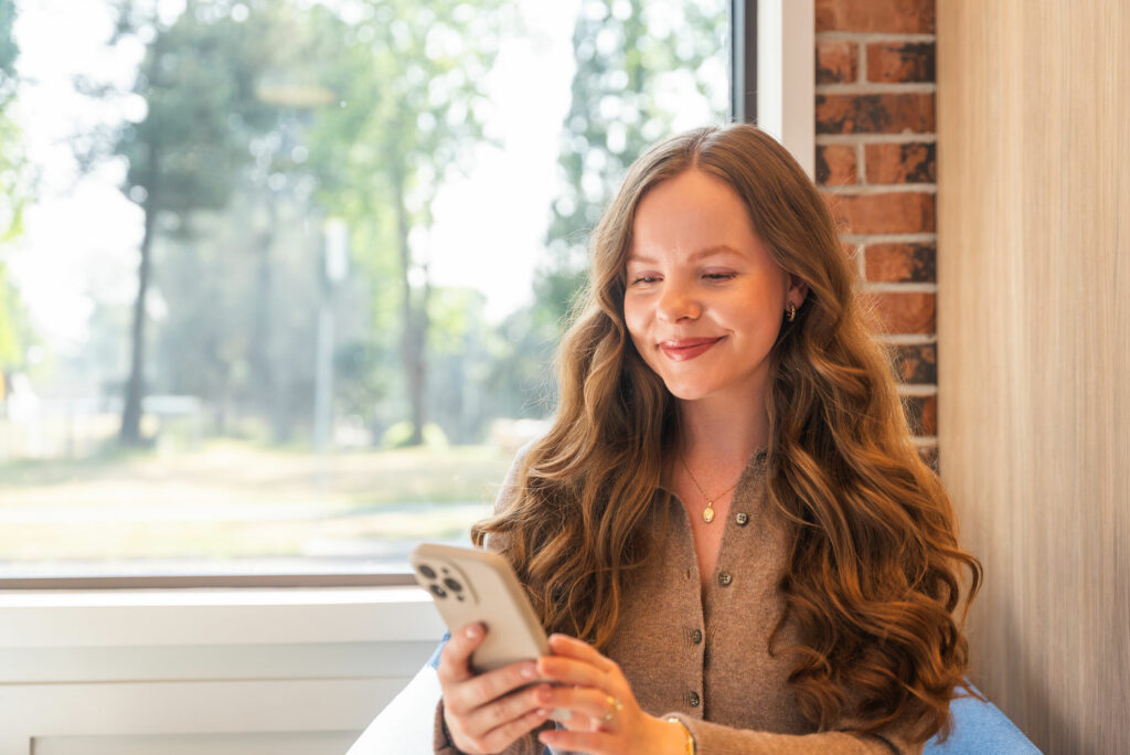 Libro Owner, Kennedy, looking at her phone and smiling sitting in a Libro branch.