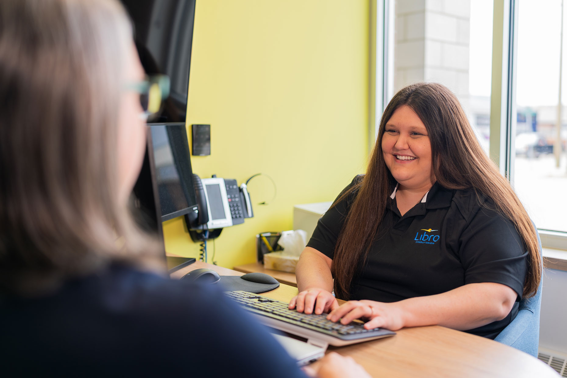 Libro Watford Staff Member sitting behind a desk and smiling at a Libro Owner