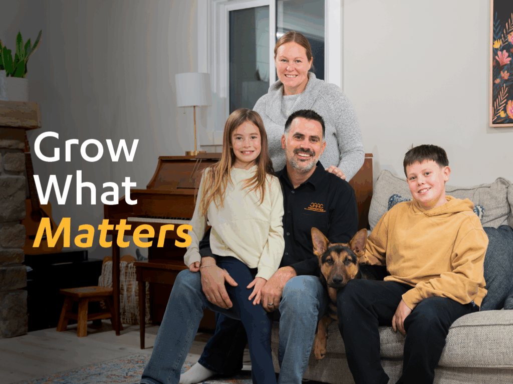 A smiling family of four and a dog pose together in a living room near a piano, with the text 